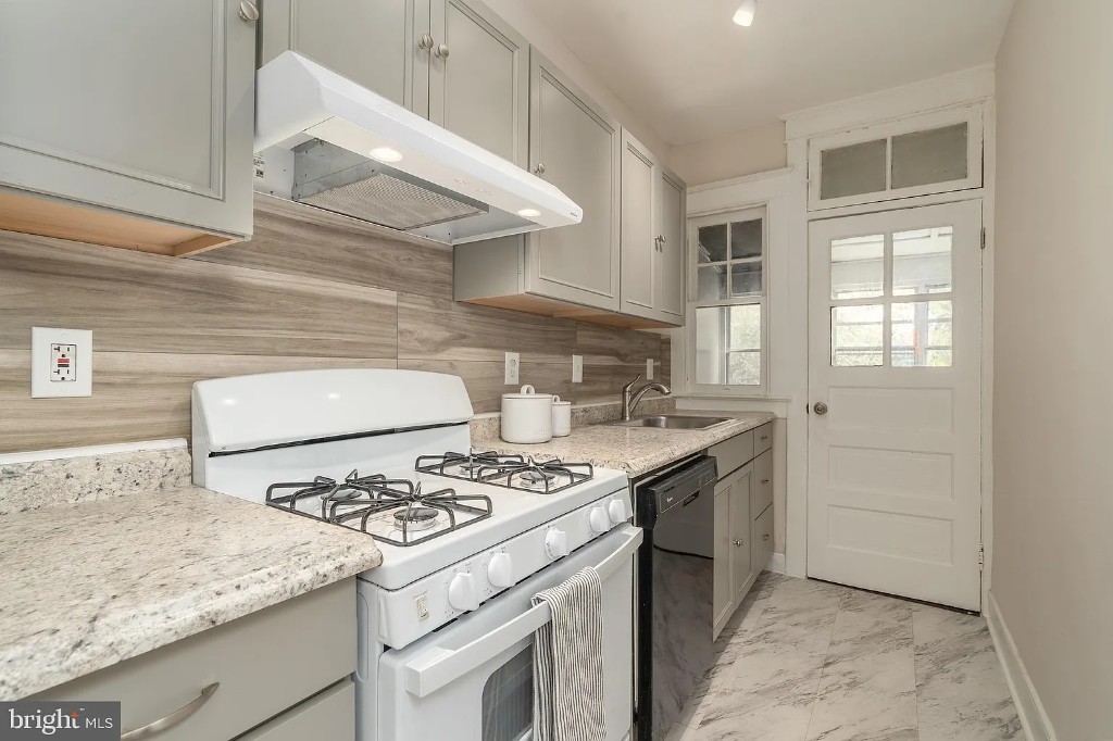 Renovated kitchen with light gray cabinets, speckled countertops, and wood-look tile backsplash