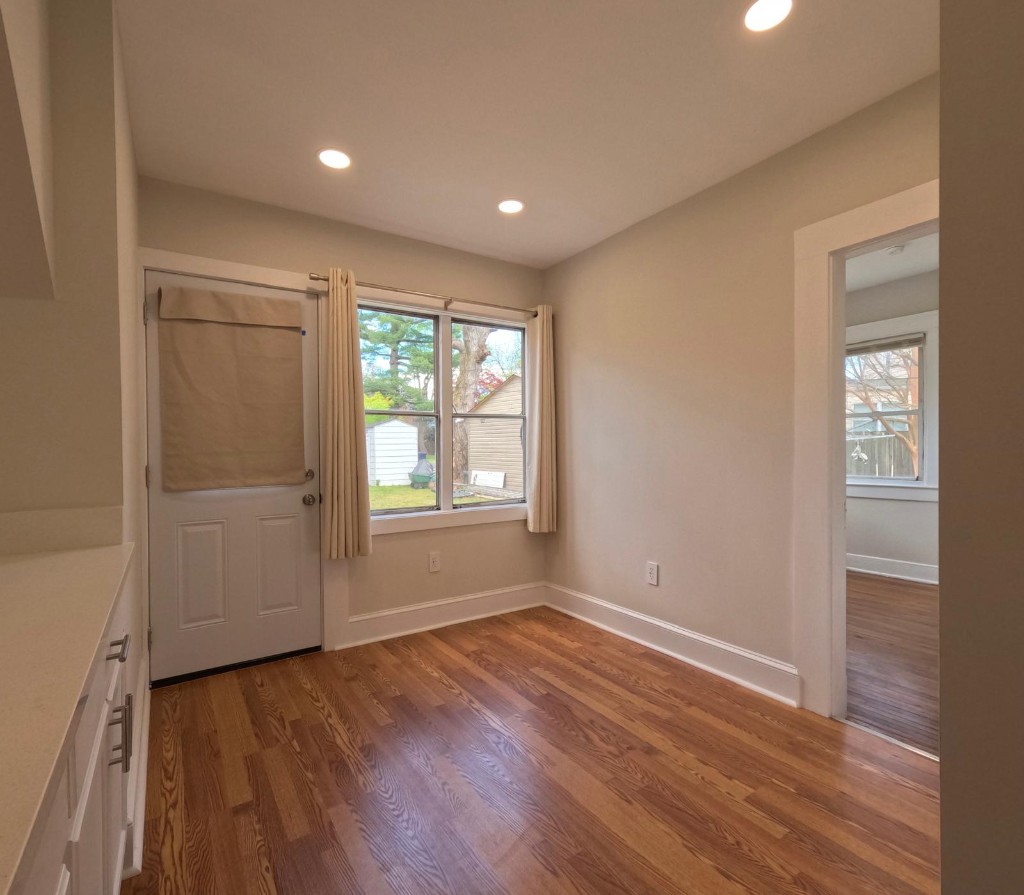 Bright side room with hardwoods, door and window opening to a backyard with lawn and tree