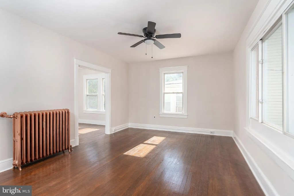 Spacious room with dark hardwood floors, light walls, large windows, and a vintage radiator